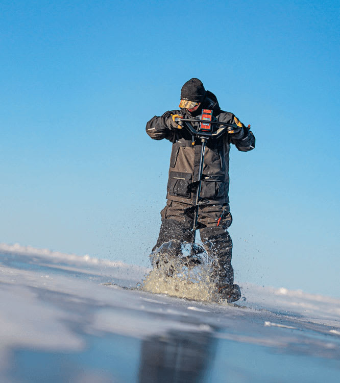 Eisangler in Thermoausruestung geht ueber eine zugefrorene Flaeche.