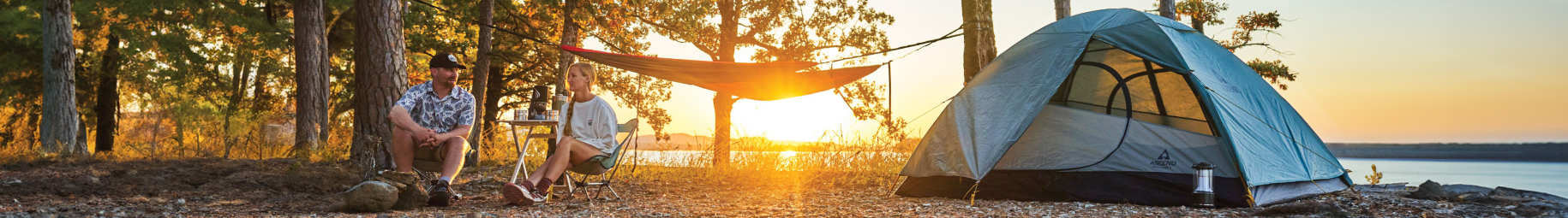 Campsite at a lake at sunset with a dome tent, hammock and two camp chairs