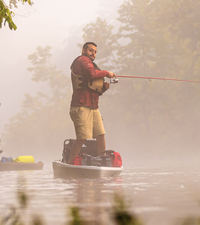 Angler wirft stehend von einem Kajak im Morgennebel aus.