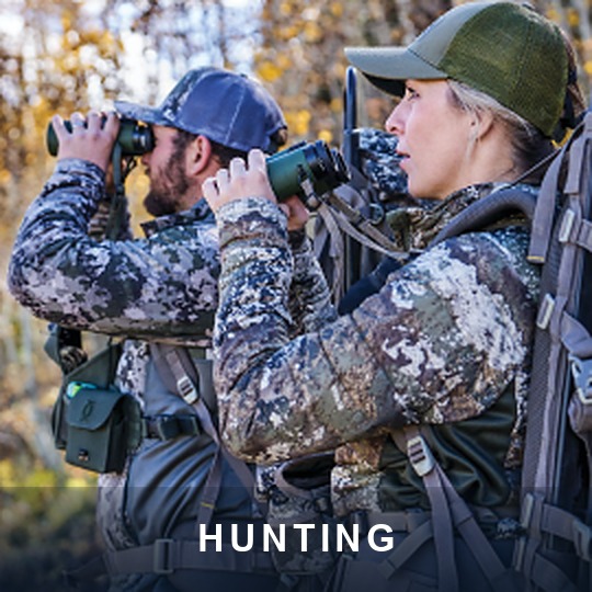 Two hunters in camouflage glassing with binoculars in autumn backcountry, caption HUNTING