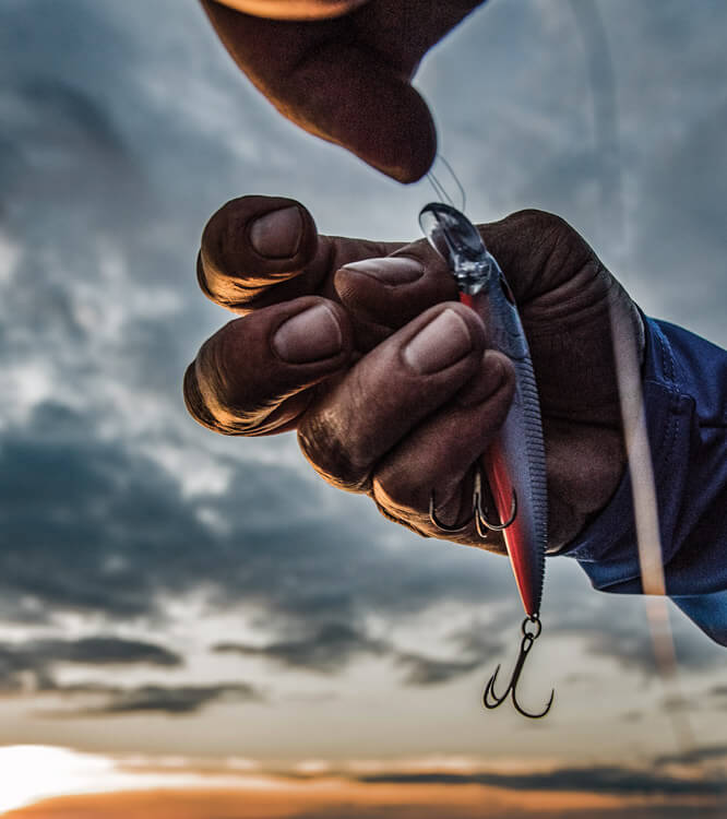 Behandschuhte Hand haelt einen Wobbler mit Drilling.