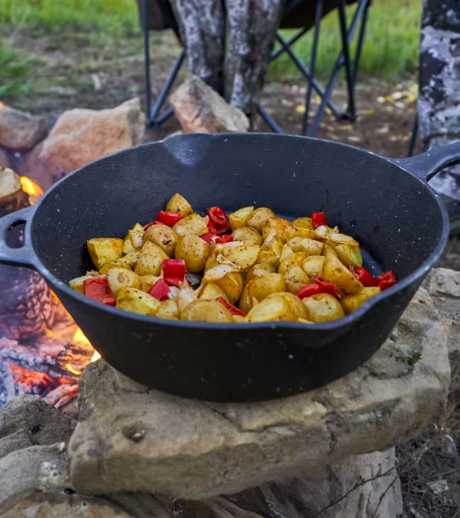 Cast iron skillet with roasted potatoes and peppers on a campfire ring