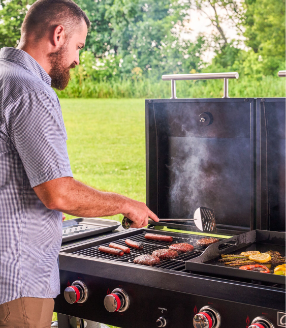 Person grilling sausages, burgers and vegetables on an outdoor gas grill